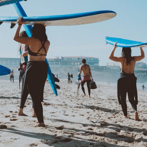 Women carrying surfboards on a sunny beach, enjoying a day of surfing and recreation.