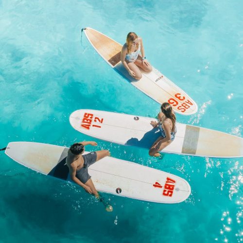 Three surfers resting on their boards in crystal clear Hawaiian waters, showcasing vibrant ocean life.
